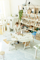 View of small modern workroom and table where young woman in kimono making clay toys and souvenirs for sale