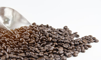 The group of roasted coffee beans with stainless spoon put on white background,blurry light around.