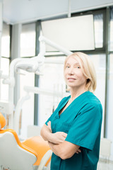 Female dentist or assistant in uniform crossing her arms on chest while looking at camera