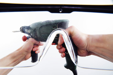 View of men's hands with an electric drill through protective glasses. First-person view.