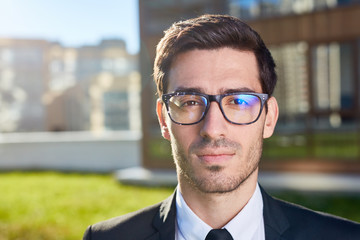 Young businessman in eyeglasses and formalwear looking at camera in urban environment