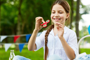 Happy and carefree girl in white cotton blouse playing with fidget spinner in park on summer day