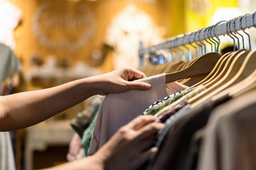 Close up of woman hand choosing thrift young and discount t-shirt clothes in store, searching or...