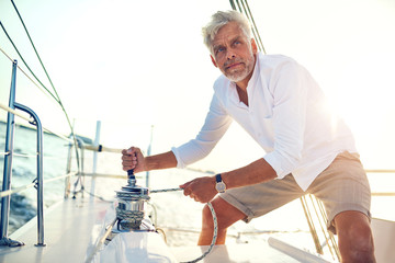 Mature man standing on his boat using a winch