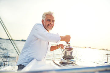 Mature man working a rope winch on his sailboat