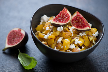 Pumpkin salad with cheese, pistachios and fig fruits served in a black bowl, studio shot