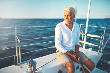 Smiling mature man sailing his yacht on a sunny day - obrazy, fototapety, plakaty