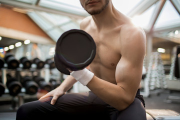 Fototapeta premium Muscular young man exercising with heavy barbell in one hand while training in sports center
