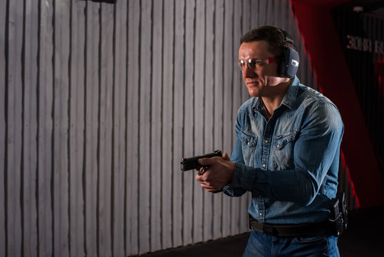 An adult man in jeans trains to shoot a gun in a closed dash.