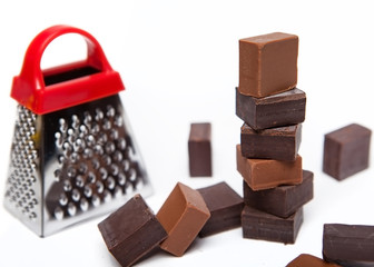 Black and milk chocolate cubes next to grater on white background