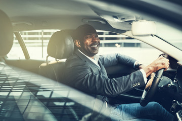 Smiling African businessman driving through city traffic