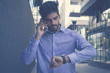  Worried businessman using phone and checking the time outdoors.