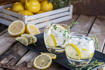 Lemon cocktail with thyme and ice on dark rustic background, close-up. Refreshing alcoholic yellow cocktail drink.