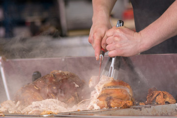 man carving pork joint with fork and knife at hog roast