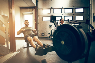 Fit young people working out on gym rowing machines