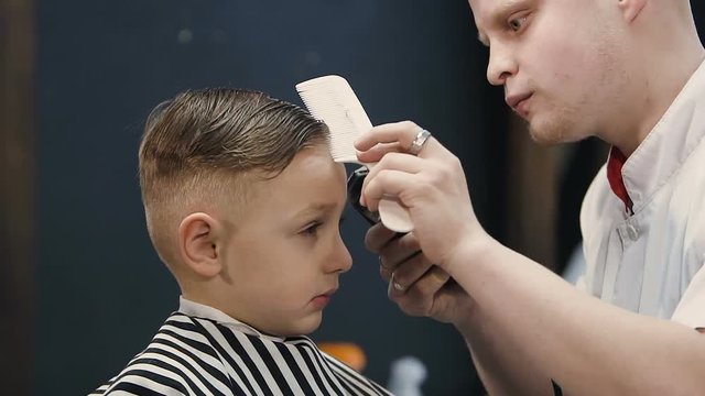 Hairdresser making hair cut for little boy. machine. Barber cutting hair with hair trimmer and hairbrush. Child haircut with comb and razor. New hairstyle for the beautiful boy