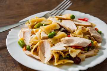 farfalle pasta salad with chicken breast fillet and vegetables in plate on wooden background