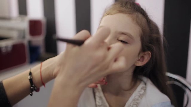 The girl is a master makeup artist who paints her lips on a model little girl.