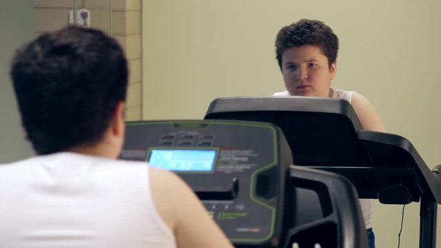 tired little fat cute boy walking on treadmill in the gym indoors