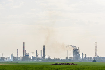 View of an oil refinery with smoking chimneys releasing toxic gases in the air, surrounded by crop...