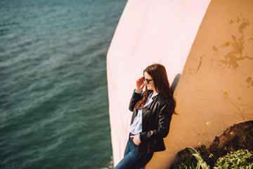 Beautiful girl with sunglasses rests against the yellow wall. In the background, the beautiful sunset and the beginning of the sunset