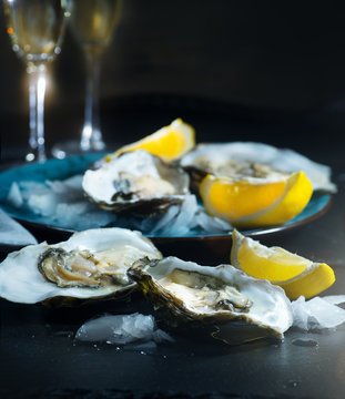 Fresh Oysters closeup on blue plate, served table with oysters, lemon and ice. Healthy sea food. Oyster dinner with champagne in restaurant. Gourmet food
