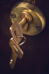 closeup of pair of keys in wooden door lock
