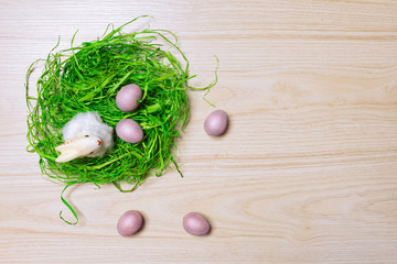 Easter decorations on wooden background with grass, rabbit and eggs. Top view.