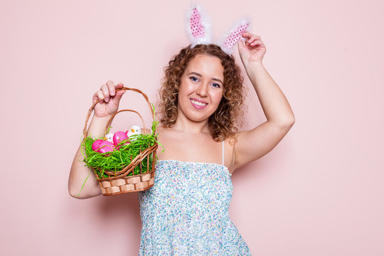 Beautiful woman hold easter decorations with bunny ears on pink color background with copy space.