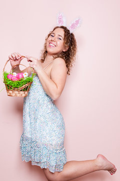 Beautiful woman hold easter decorations with bunny ears on pink color background with copy space.