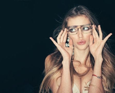 Woman attractive with big breasts wears ugly eyeglasses for vision. Sexy girl with makeup and big earrings, dark background. Optics store concept. Girl short sightedness needs modern eyeglasses.