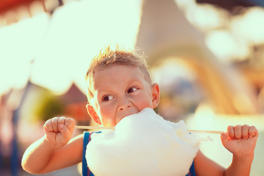 Young boy standing and biting candy cotton on the street in sunny day.