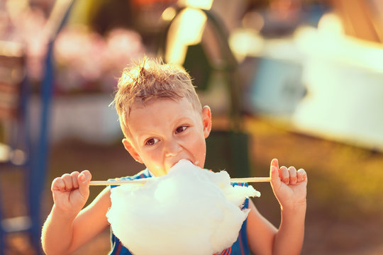 Young boy standing and biting candy cotton on the street in sunny day.