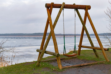 old wooden swing on the grass with view of the water and sky. Off into the wild blue yonder. Alone