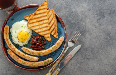 Traditional full English breakfast with fried eggs, sausages and beans on grey background. Top view
