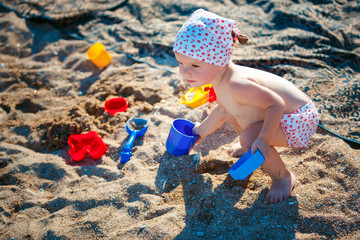 Cute little girl sitting on the beach and playing with plastic toys.