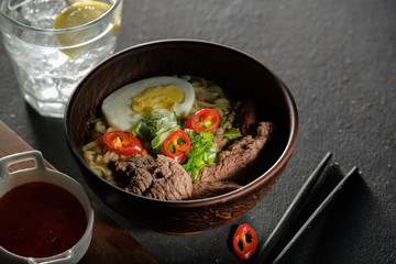 Asian ramen soup with beef, egg, chives in bowl on grey background.