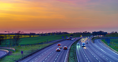 Colourful sunset at M1 motorway near Flitwick junction with blurry cars in United Kingdom - obrazy, fototapety, plakaty