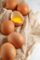 brown hen's eggs one egg yolk visible decorated on napkin, rustic food photography on white wood can be used as background
