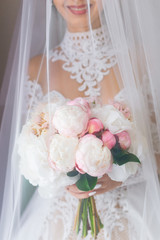 elegant bride in a beautiful dress holds a wedding bouquet and covered with veil