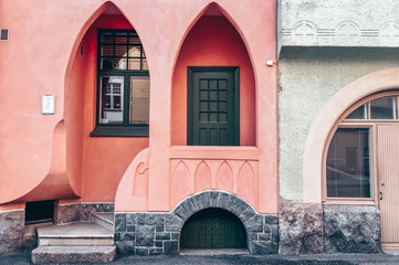 The facade of a Jugendstil building. Unique pink house with an arched doorway entrance and green...