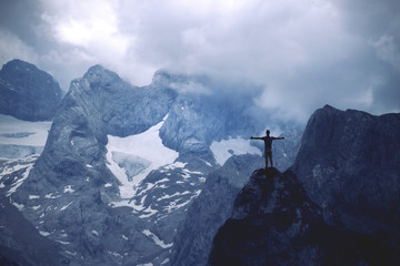 Man standing on a mountain top with raised hands above the cloudy valley
