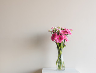 Close up of pink gerberas and carnations in glass vase on small table against neutral wall background with copy space