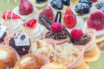 Different sort of small sweet cakes with vanilla, chocolate, strawberry, blackberry and sugar powder