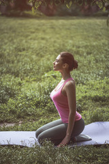 Full length side view serene girl expressing tranquility while meditating on mat in grass. Calm lady demonstrating composure during physical exercise concept