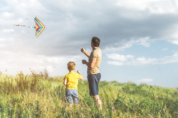 Adult male and his little son are standing on grassland and flying a kite. Copy space in right side