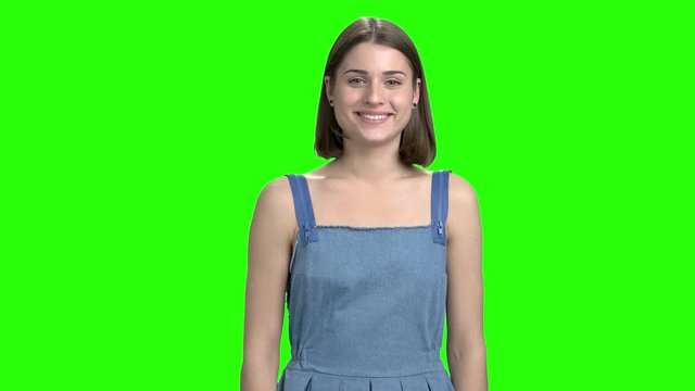 Cheerful smiling woman in denim dress flirting on camera. Front view, cute brunette girl. Green screen hromakey background for keying.