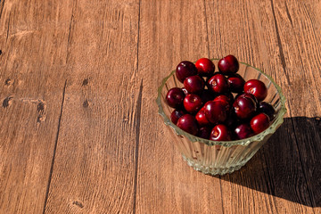 Berries of a sweet cherry in a glass bowl on a wooden background. Ripe red sweet cherry