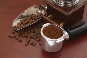Coffee machine portafilter with ground coffee and roasted coffee beans, vintage manual grinder and shovel on wooden table
