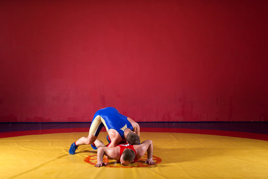 Two greco-roman  wrestlers in red and blue uniform wrestling   on a yellow wrestling carpet in the gym